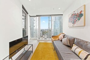 A modern living room with a sofa, a yellow rug, and a large window with a city view. - A Lux & Cozy Apt Next to Southern Cross Station (Melbourne)