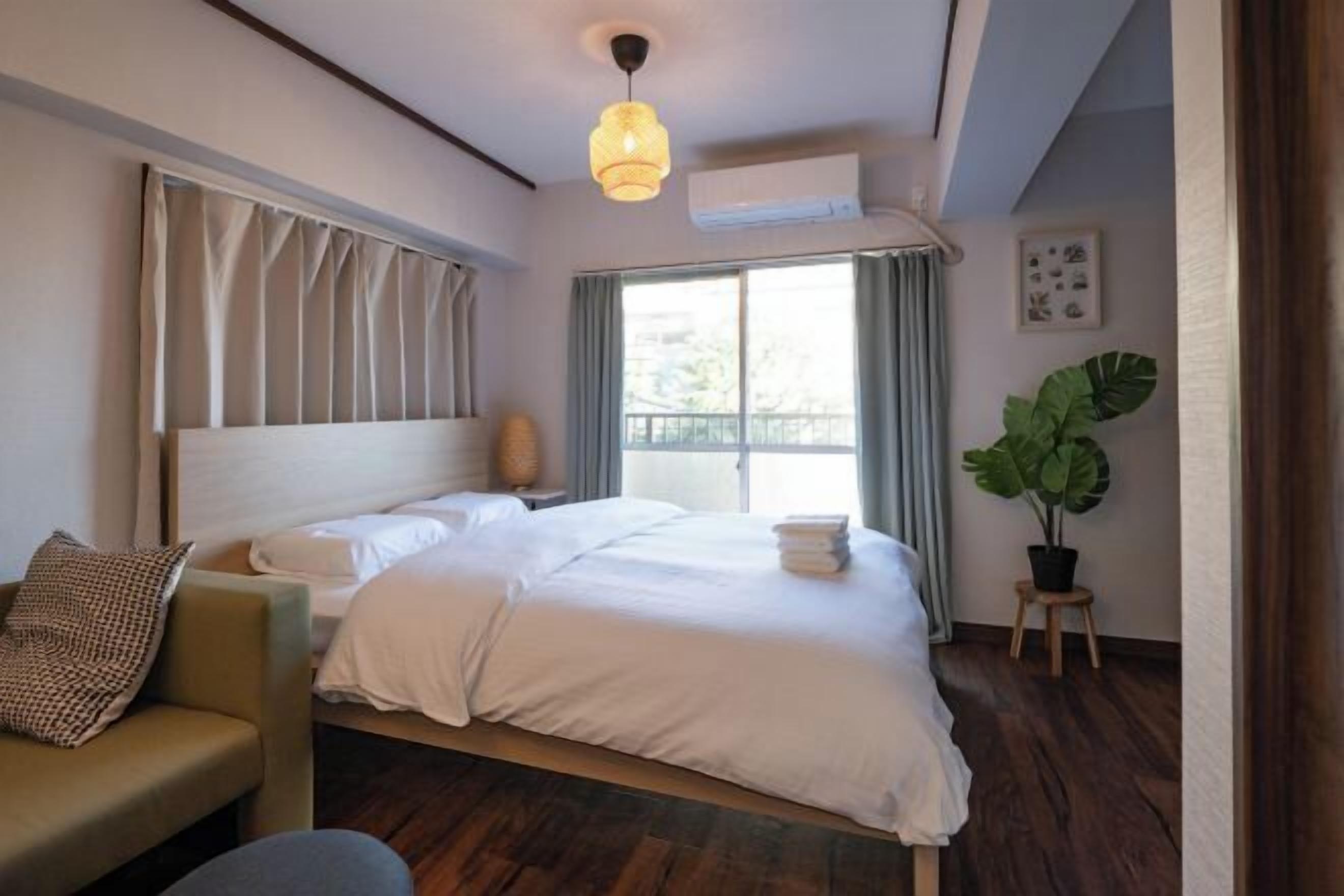 A hotel room with a large bed, a sofa, a potted plant, and a window with curtains.