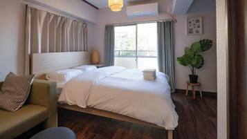 A hotel room with a large bed, a sofa, a potted plant, and a window with curtains.