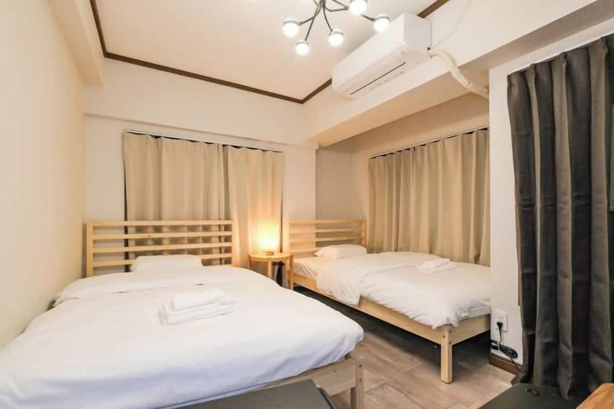 Habitación de hotel con dos camas individuales, cabecera de madera, unidad de aire acondicionado y lámpara en el techo.