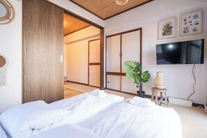 Een hotelkamer met een bed, een televisie, een kamerplant en een schuifdeur die naar een andere kamer leidt.