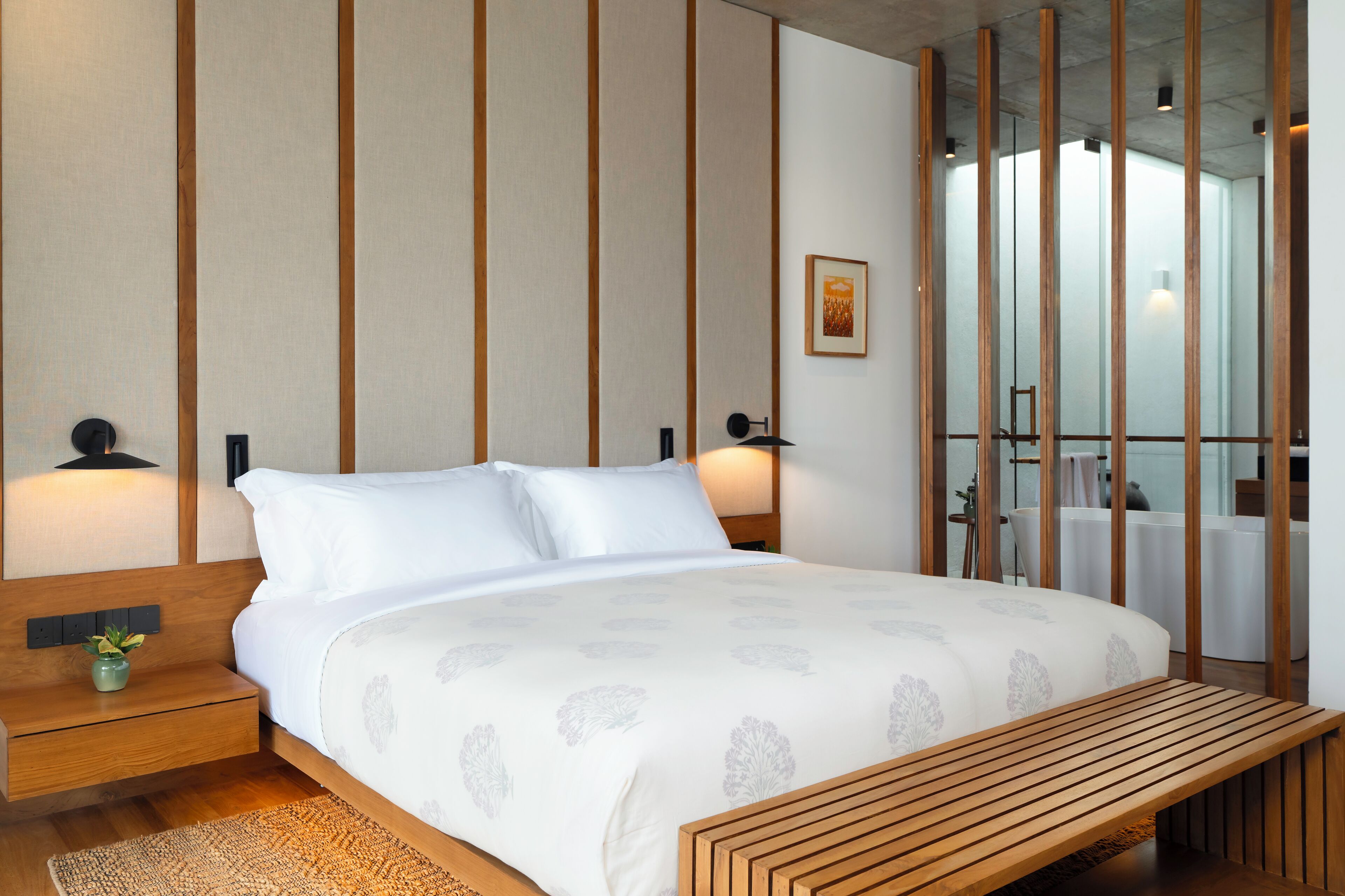 A modern bedroom with a large bed, wooden headboard, bedside tables, and a bench.