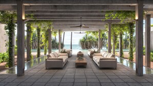 A covered outdoor seating area with sofas and a coffee table, overlooking a pool and the ocean. - Nyne Hotels Anugrah - Bentota (Bentota)
