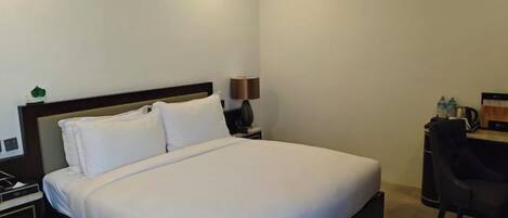 A hotel room with a bed, bedside table, lamp, and a desk with a chair.