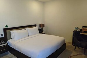 A hotel room with a bed, bedside table, lamp, and a desk with a chair. - Huadu Hotel (Kathmandu)