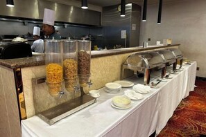 A buffet setup with multiple food dispensers and a long table with plates and bowls. - Huadu Hotel (Kathmandu)