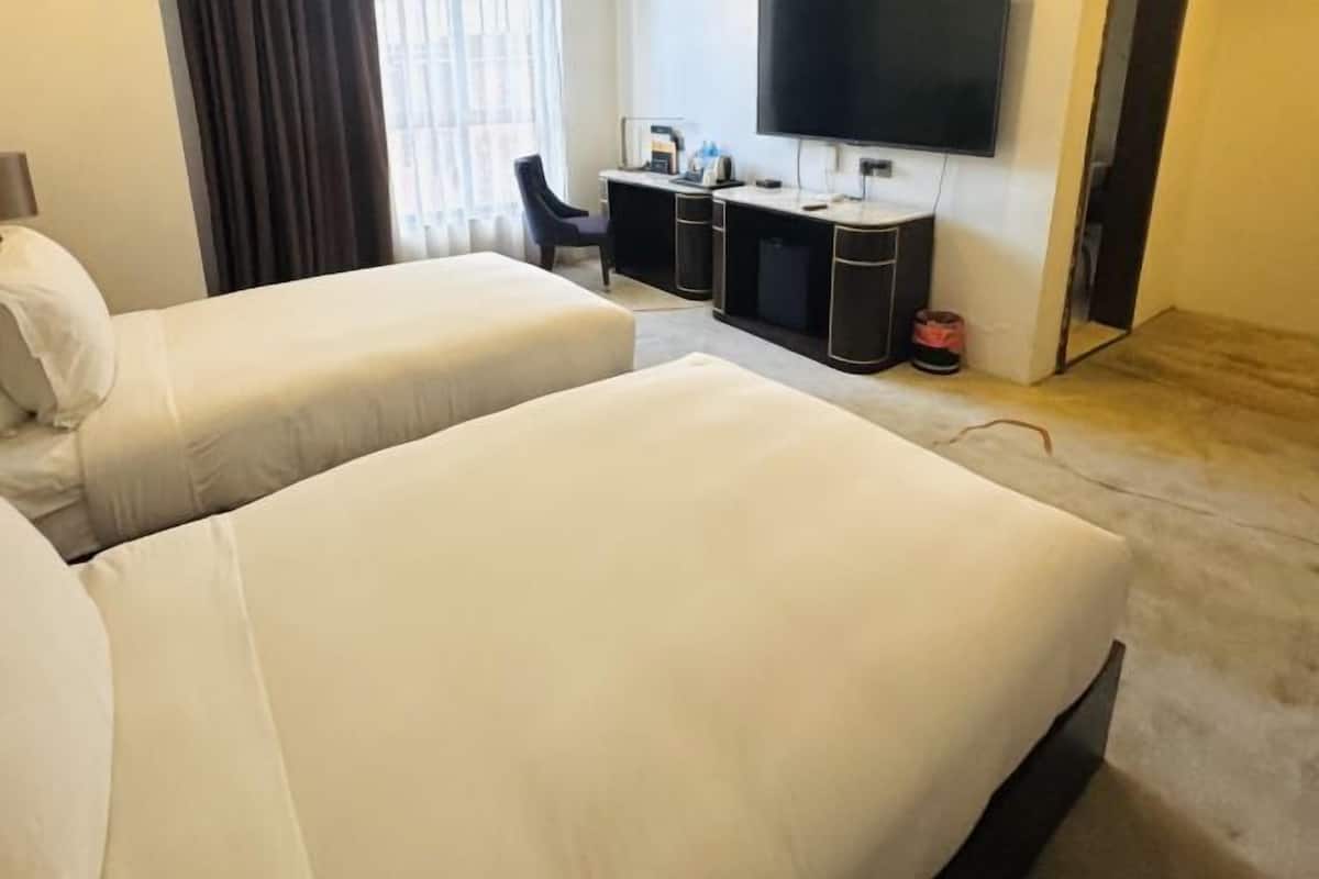 Une chambre d’hôtel avec deux lits, un bureau, un téléviseur à écran plat et une petite poubelle.