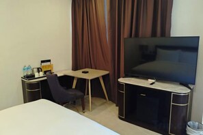 A hotel room with a bed, a desk with a chair, a TV, and a small table. - Huadu Hotel (Kathmandu)