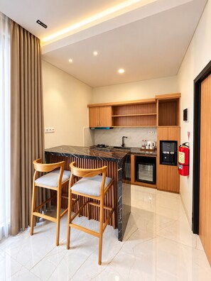 A modern kitchen with a marble countertop, wooden cabinets, and a built-in mini-fridge. There are two wooden chairs with cushioned seats. - Lakeside Tell Cikarang (Serang Baru)