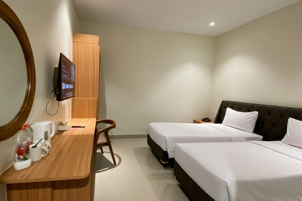 A hotel room with two beds, a desk with a chair, a large mirror, and a television mounted on the wall.