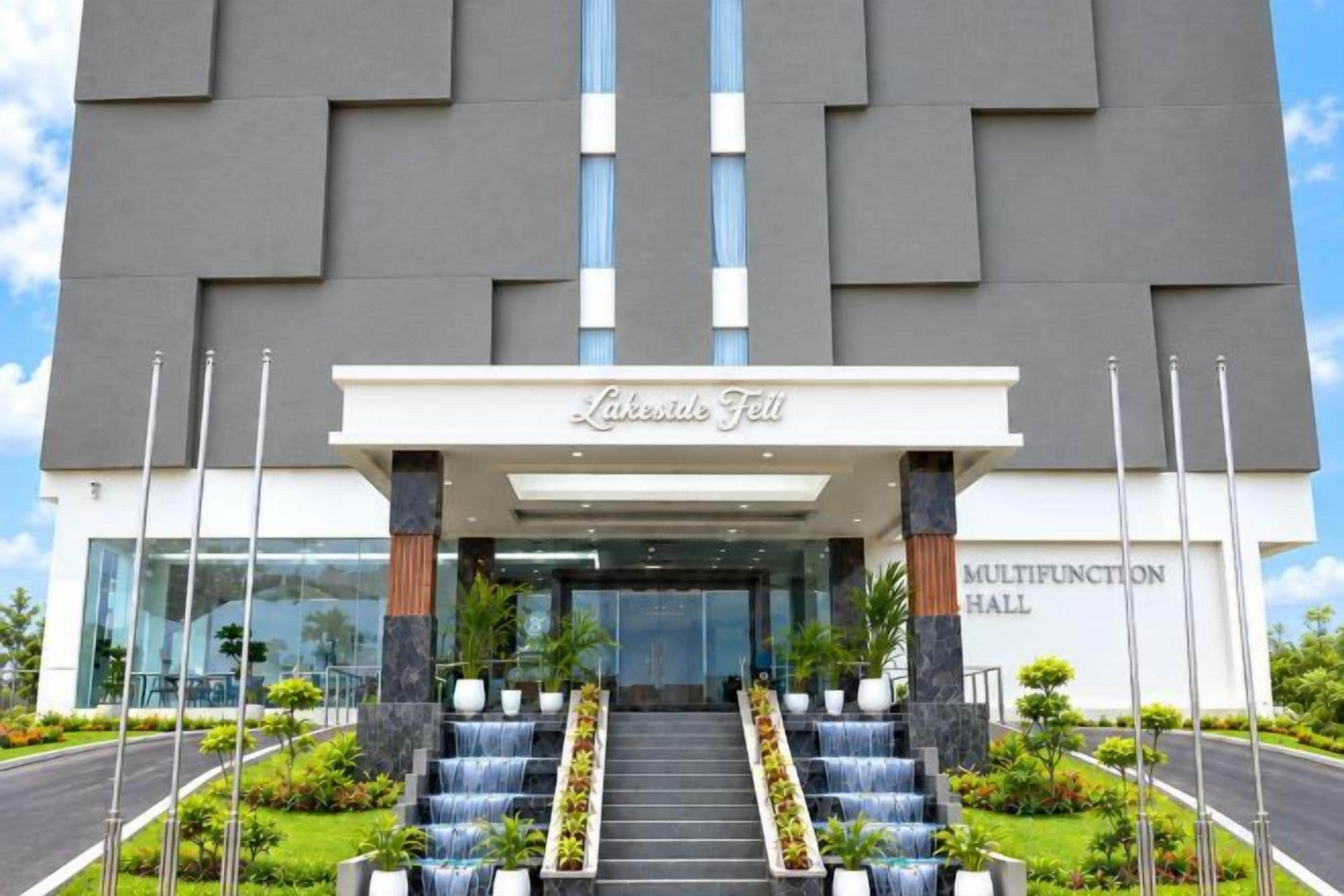 A hotel entrance with a name sign, a staircase leading up to the entrance, and a landscaped area with plants.