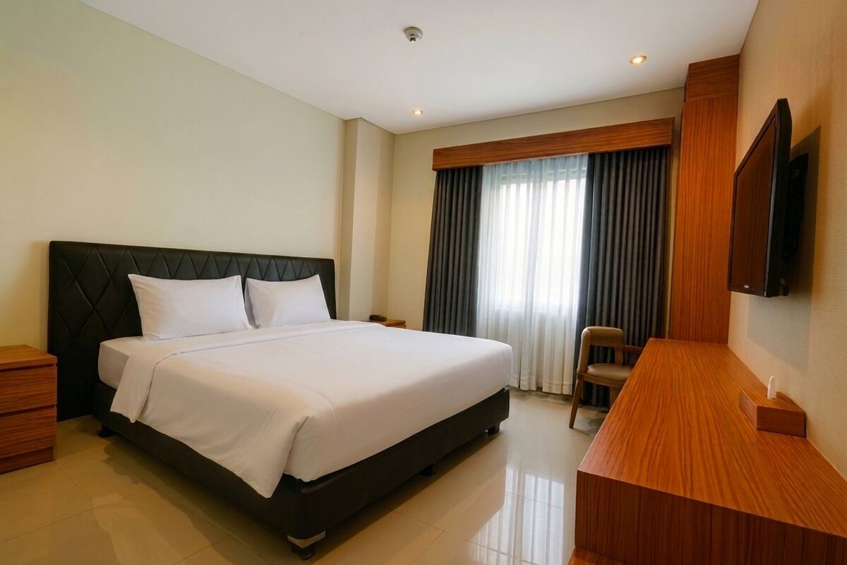 Une chambre d’hôtel avec un grand lit, un bureau, une chaise, une télévision et une fenêtre avec des rideaux.