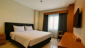 A hotel room with a bed, a desk, a chair, a television, and a window with curtains. - Lakeside Tell Cikarang (Serang Baru)