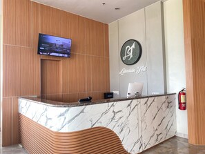 Un taulell de recepció amb encimera de marbre, un televisor de pantalla plana penjat a la paret i un extintor a la dreta.