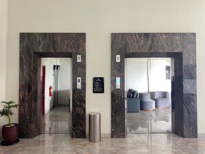 A hotel lobby with marble walls, a reception desk, a trash bin, and a seating area with sofas. - Lakeside Tell Cikarang (Serang Baru)