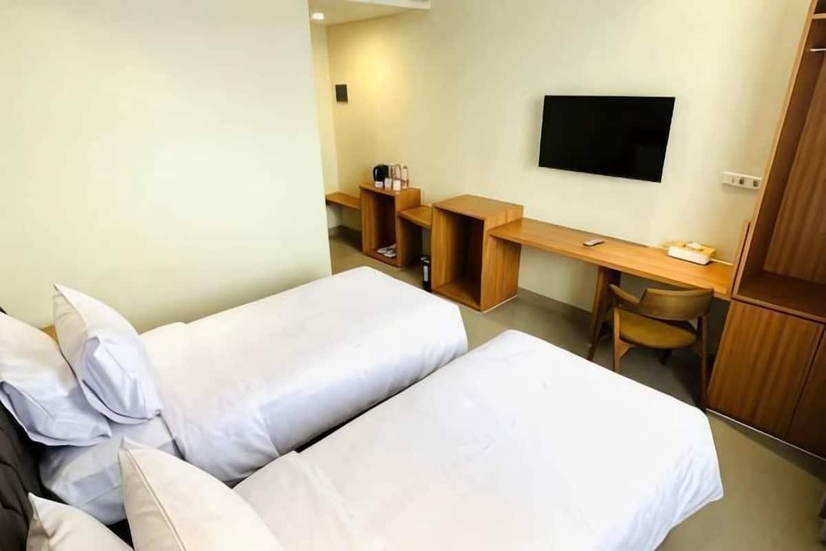 A hotel room with two beds, a desk, a chair, a TV, and a wardrobe.
