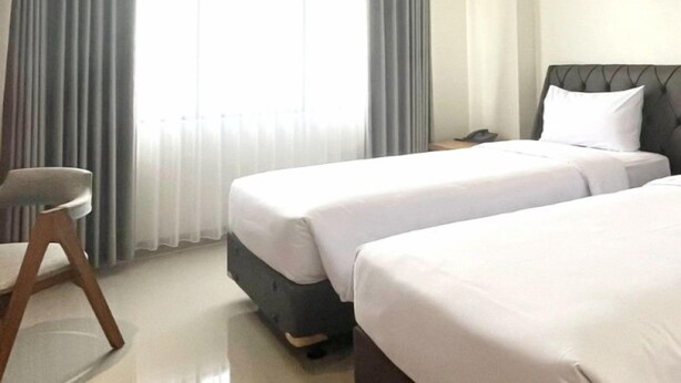 A hotel room with two beds, a chair, and a window with curtains. - Lakeside Tell Cikarang (Serang Baru)
