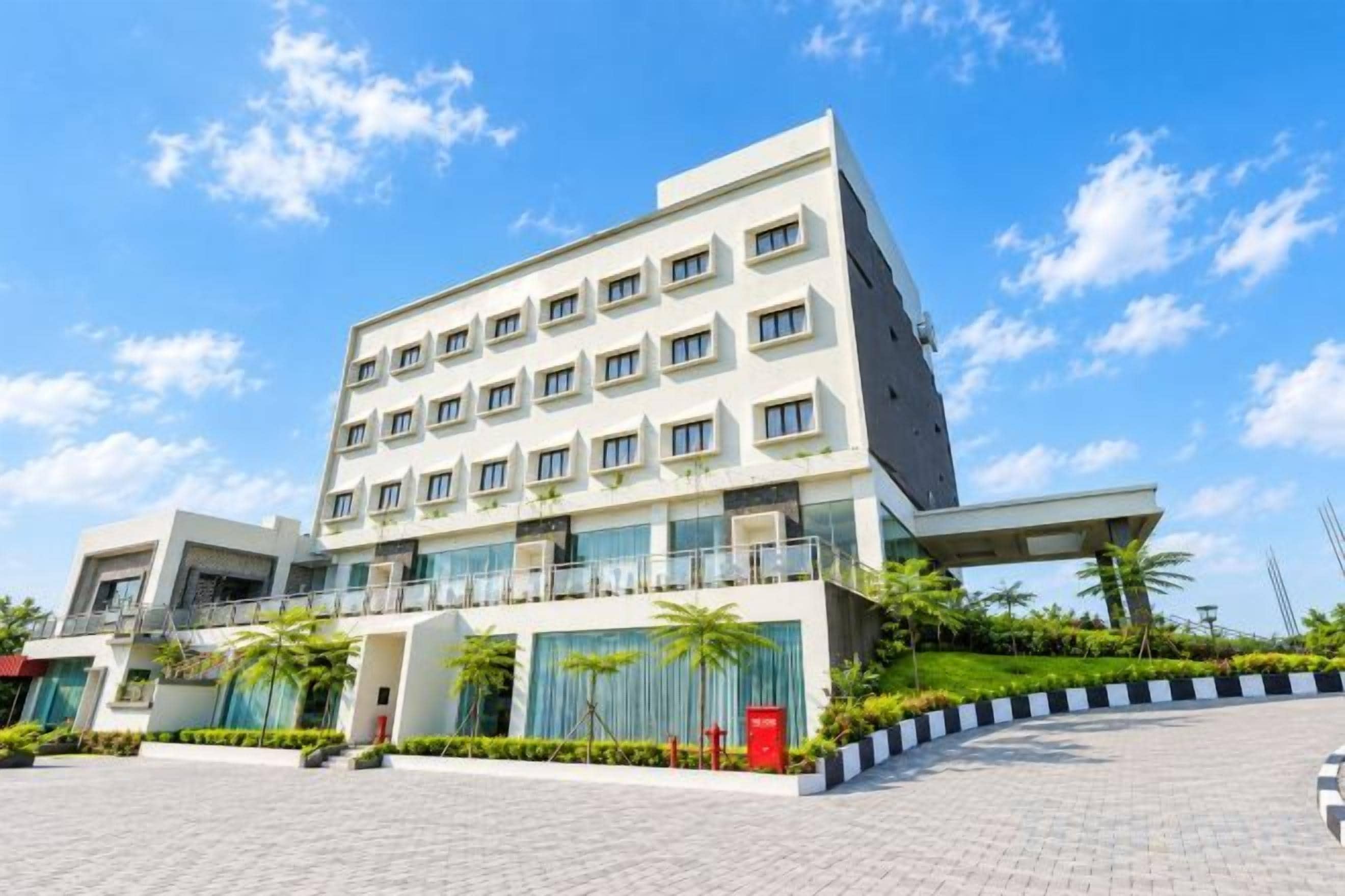 A modern hotel with a flat roof, multiple floors, and a paved courtyard.
