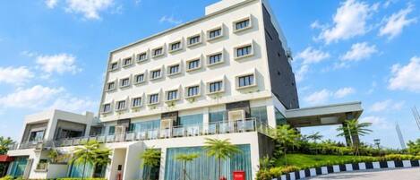 A modern hotel with a flat roof, multiple floors, and a paved courtyard.