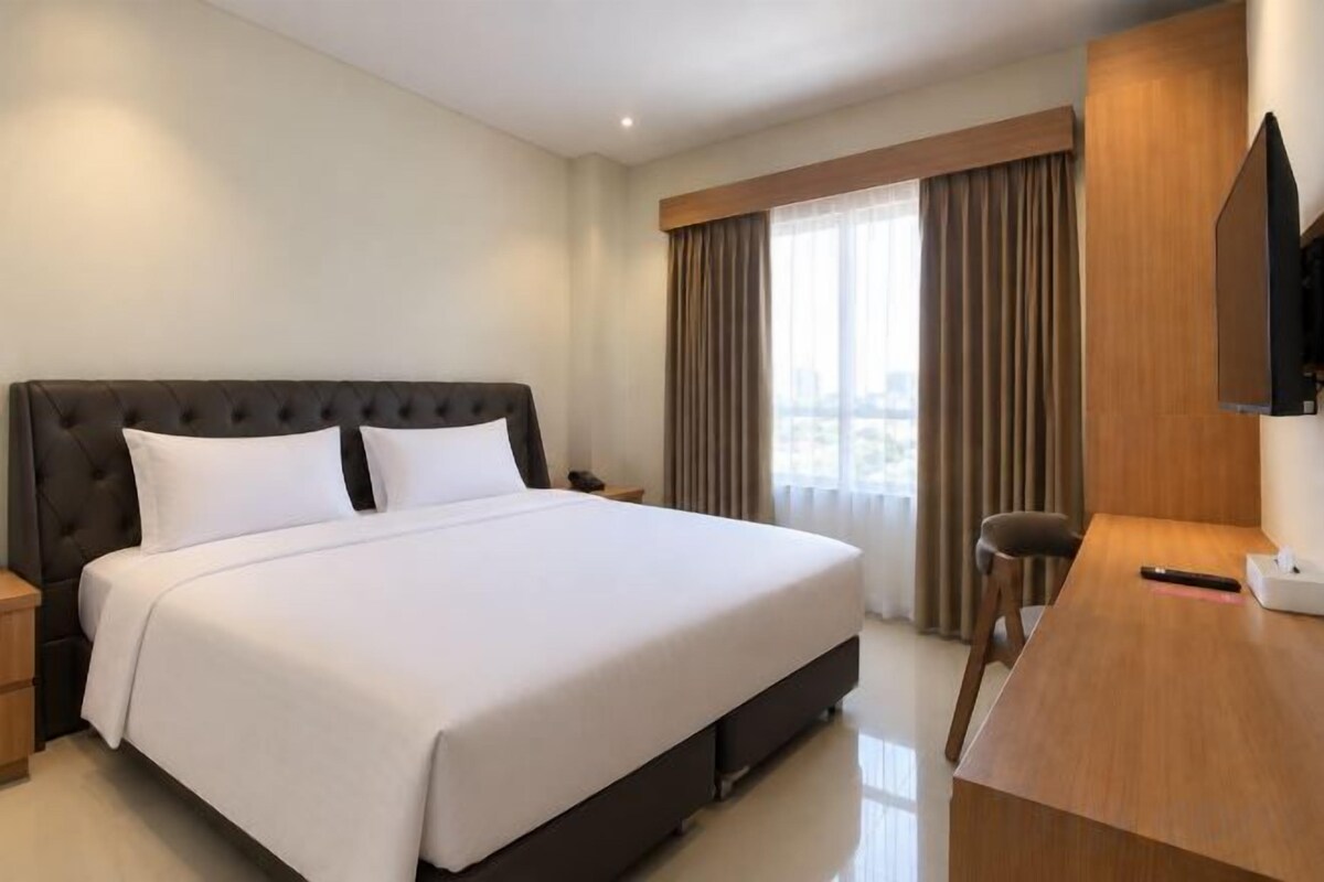 A hotel room with a large bed, a desk, a chair, a TV, and a window with curtains.