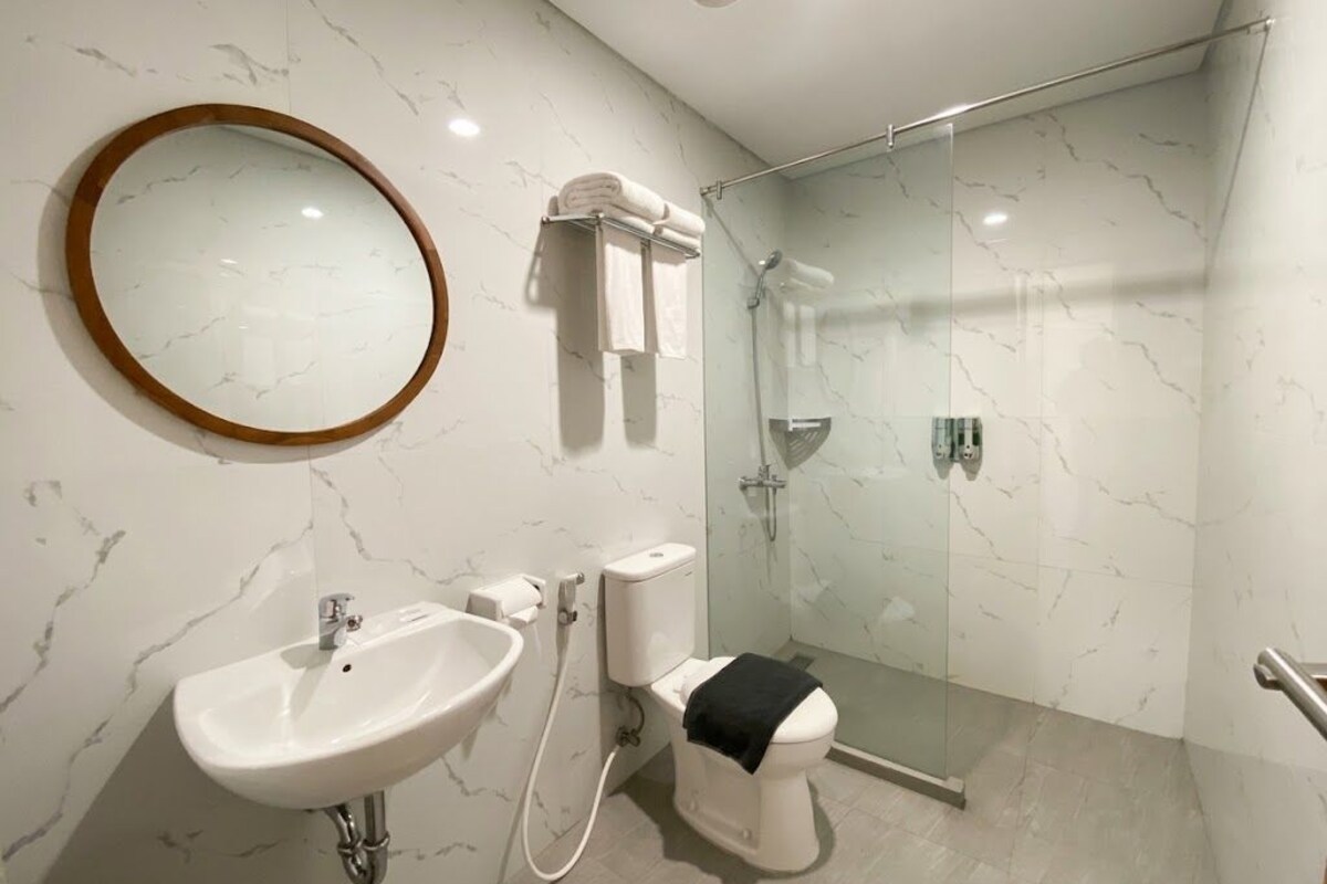 A modern bathroom with a marble wall, a round mirror, a sink, a toilet, and a glass shower enclosure.
