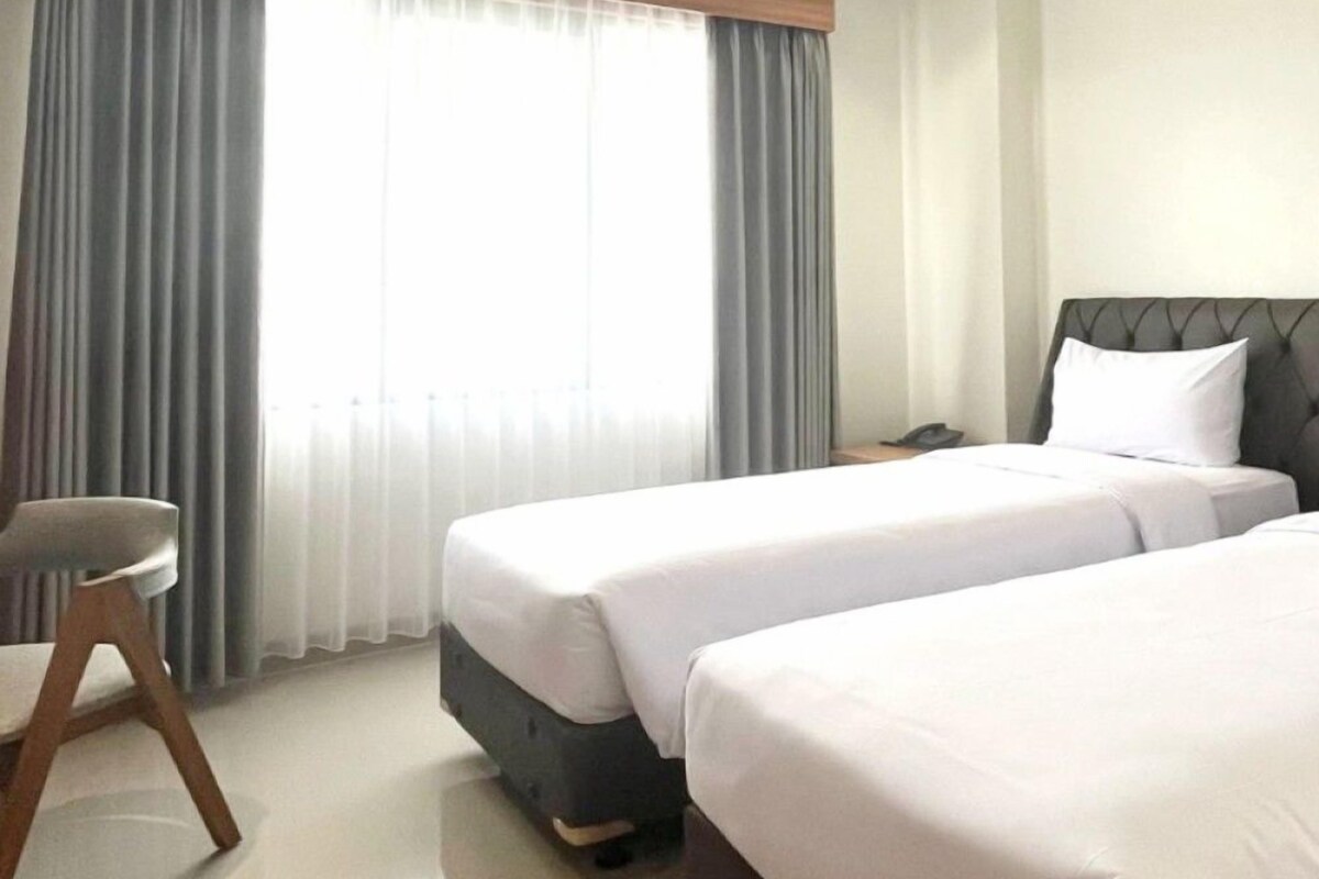 Une chambre d’hôtel avec deux lits, une chaise et une fenêtre avec des rideaux.