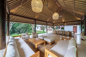 An open-air lounge with wooden furniture and a thatched roof. - VillaJewel Bali (Bali)