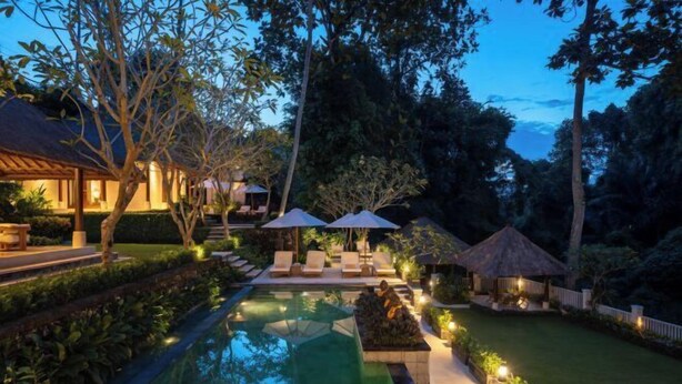 A serene pool area with lounge chairs and umbrellas, surrounded by lush greenery and a thatched-roof structure. - VillaJewel Bali (Bali)