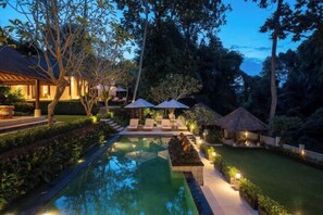 A serene pool area with lounge chairs and umbrellas, surrounded by lush greenery and a thatched-roof structure. - VillaJewel Bali (Bali)