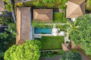 An aerial view of a resort with a swimming pool, thatched-roof structures, and lush greenery. - VillaJewel Bali (Bali)