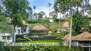 A lush, tropical garden with a white building, thatched-roof structures, and a white fence. - VillaJewel Bali (Bali)