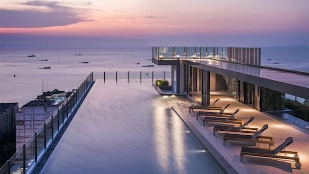 A modern rooftop terrace with a glass balustrade overlooking the sea, equipped with sun loungers and a small seating area. - Pattaya Base Seascape Apartment (Pattaya)