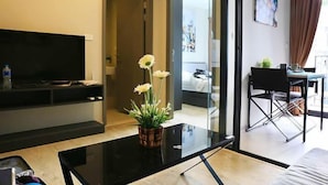A modern living room with a flat-screen TV, a glass coffee table, and a potted plant. - Pattaya Base Seascape Apartment (Pattaya)