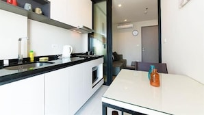 A modern kitchen with white cabinets, a black countertop, and a glass dining table. - Pattaya Base Seascape Apartment (Pattaya)