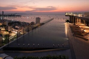 A waterfront hotel with a long, flat roof terrace overlooking the sea, a promenade, and city buildings. - Pattaya Base Seascape Apartment (Pattaya)