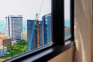 Vista desde una ventana a un sitio de construcción con grúas y edificios, con el mar al fondo.
