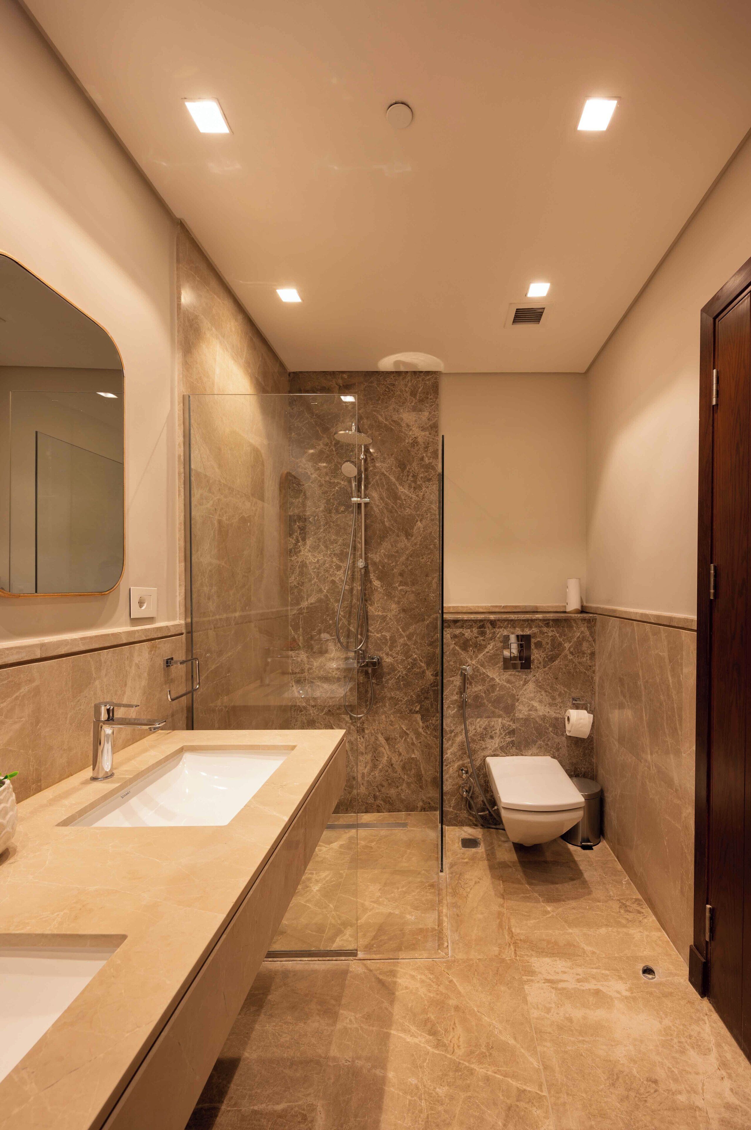 A modern bathroom with a glass-enclosed shower, a double sink vanity, and a toilet.