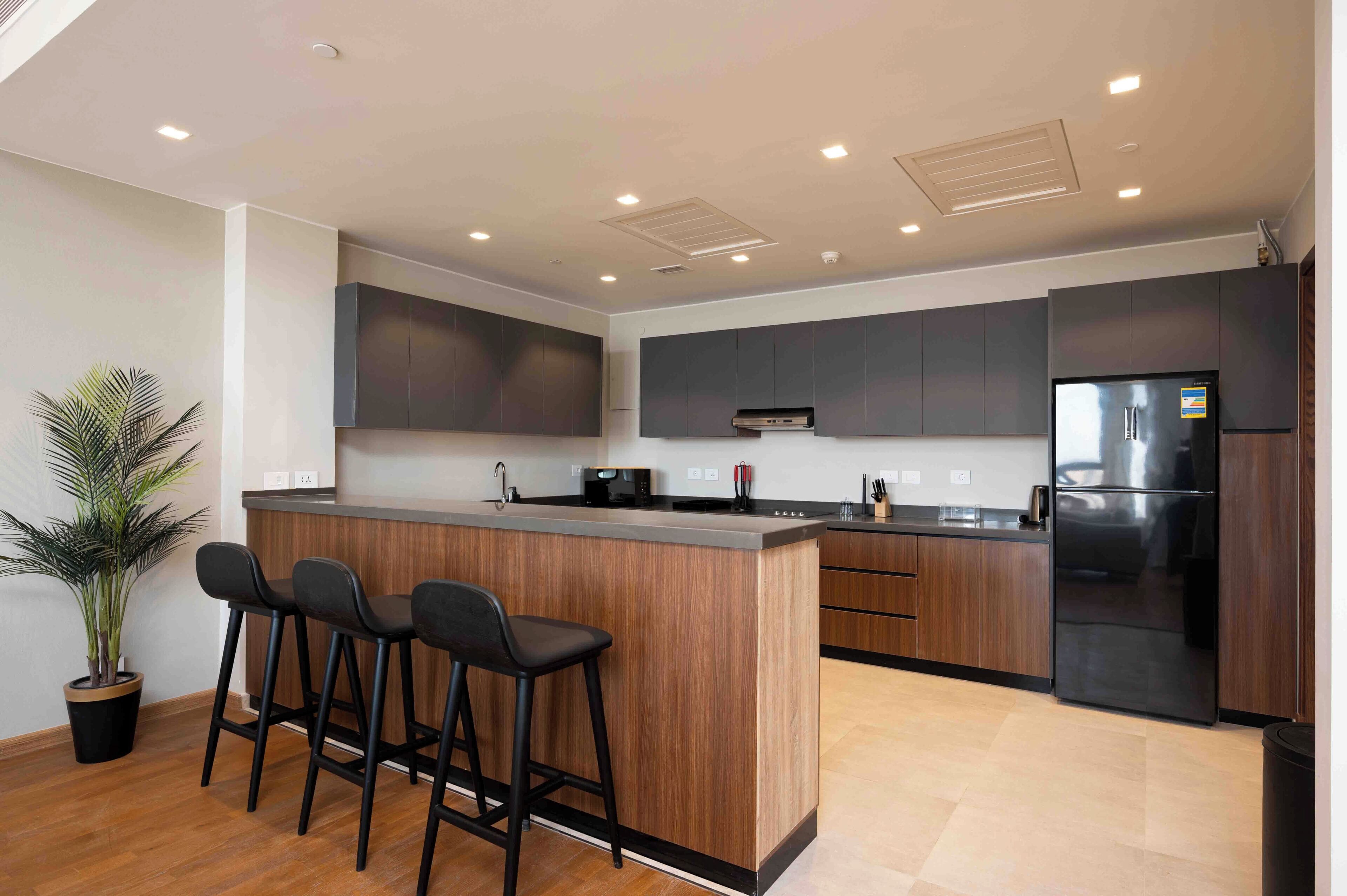 Una cocina moderna con una isla central, taburetes de bar, horno empotrado y un refrigerador de acero inoxidable.