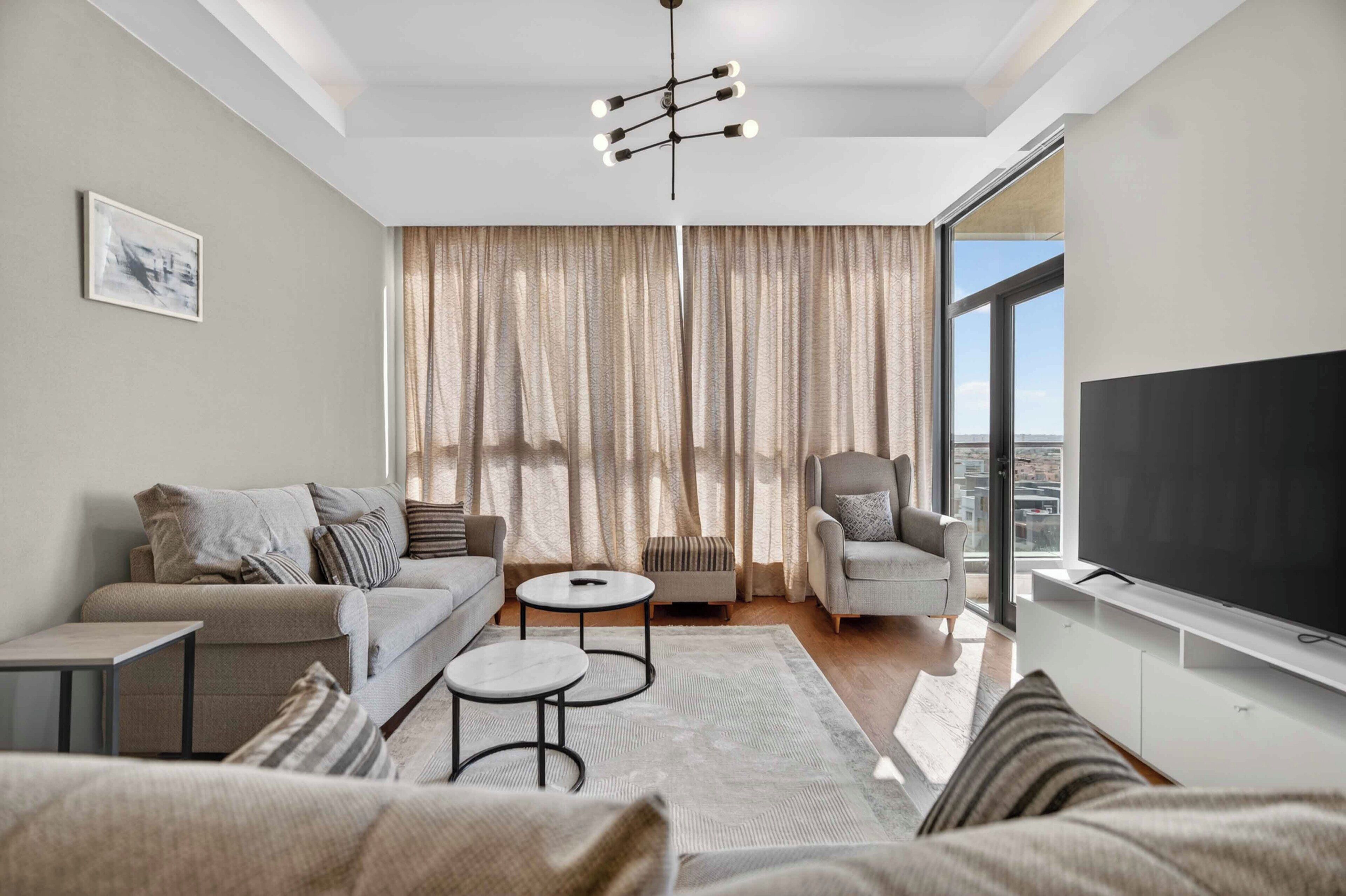 A modern living room with a sofa, armchair, coffee table, and a flat-screen TV.