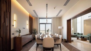 A modern dining area with a round table, chairs, and a chandelier. There is a sofa and a coffee table in the background. - Aeon Towers Residence - BirdNest (6th of October City)