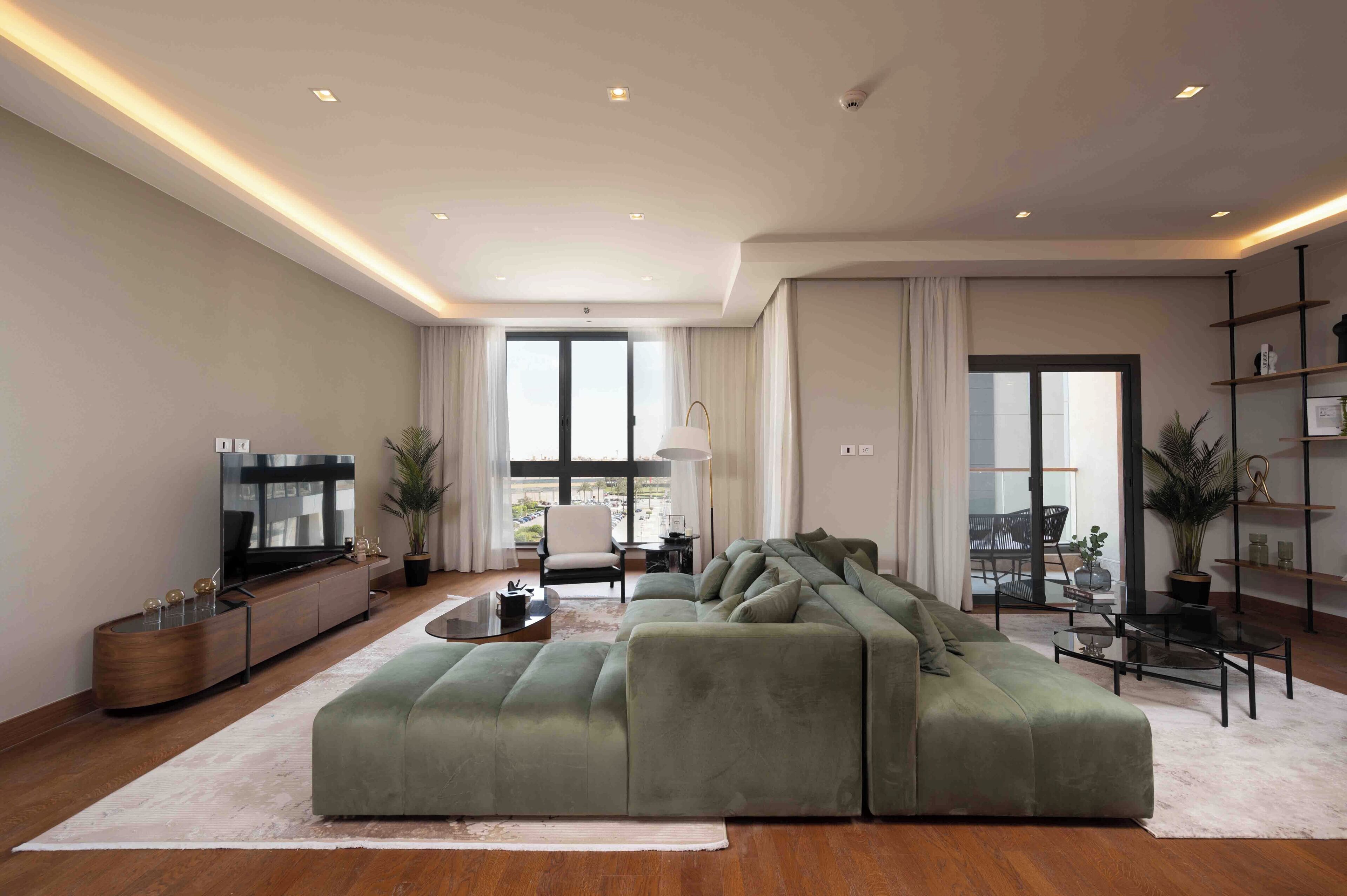 A modern living room with a large green sectional sofa, a flat-screen TV, and a minimalist decor.