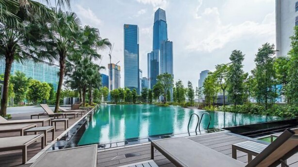 Un espace aménagé au bord de la piscine, avec des chaises longues et une vue sur les gratte-ciel modernes qui se dressent à l’arrière-plan.