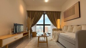 Une chambre d’hôtel moderne avec une grande fenêtre, un lit, une télévision, une table de chevet en bois et une petite table avec une lampe.