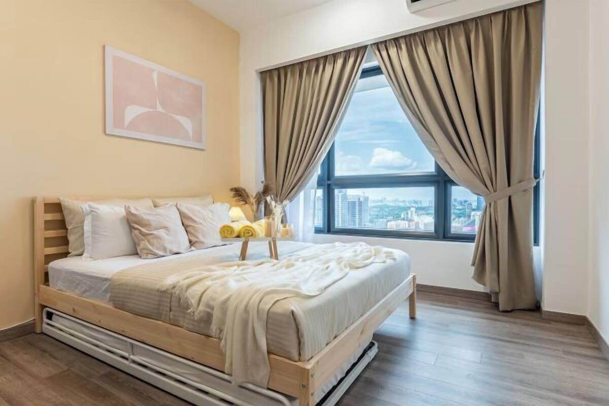 Ein Schlafzimmer mit Bett, einem Fenster mit Vorhängen, Blick auf die Stadt und einem Bild an der Wand.