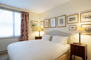 A hotel room with a large bed, two bedside tables with lamps, a window with curtains, and several framed pictures on the wall. - Artist's Oasis (London)