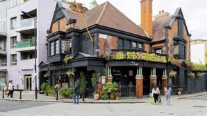 Un edificio de estilo victoriano con fachada negra, ventanas grandes y una chimenea de ladrillo.