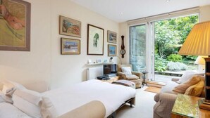 Un dormitorio con cama, sofá, televisor y ventana con vistas a la vegetación.