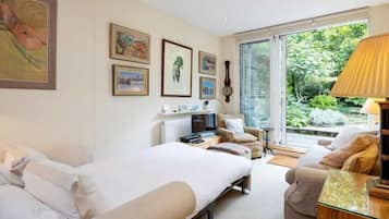 A bedroom with a bed, a sofa, a TV, and a window with a view of greenery.