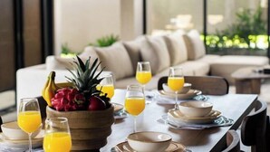 A dining table set with bowls, plates, and glasses of orange juice, with a fruit bowl containing pineapples and dragon fruit. - D'Padi Villa Canggu (Bali)