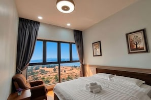 Hotelkamer met een groot bed, een bureau, een stoel en uitzicht op een landschap door een groot raam.